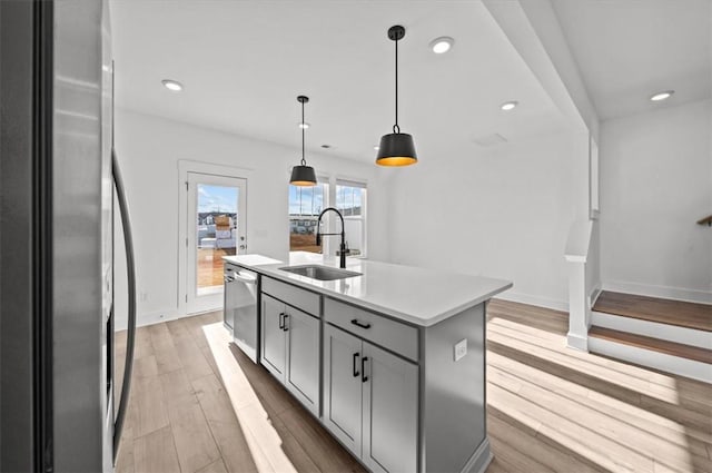 kitchen with sink, pendant lighting, a kitchen island with sink, appliances with stainless steel finishes, and light wood-type flooring