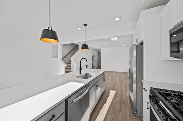 kitchen with sink, appliances with stainless steel finishes, decorative light fixtures, white cabinets, and hardwood / wood-style flooring