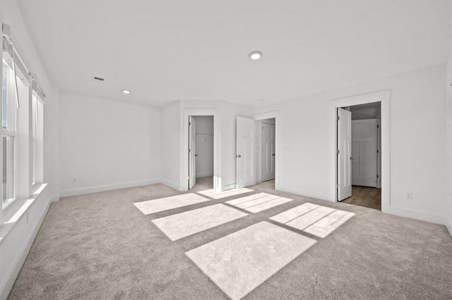 unfurnished bedroom with ensuite bath, a spacious closet, a closet, and light colored carpet