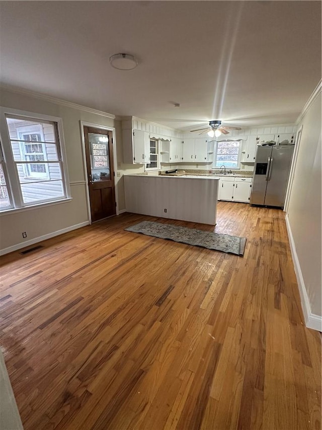 kitchen with white cabinets, stainless steel fridge with ice dispenser, ornamental molding, light hardwood / wood-style floors, and kitchen peninsula