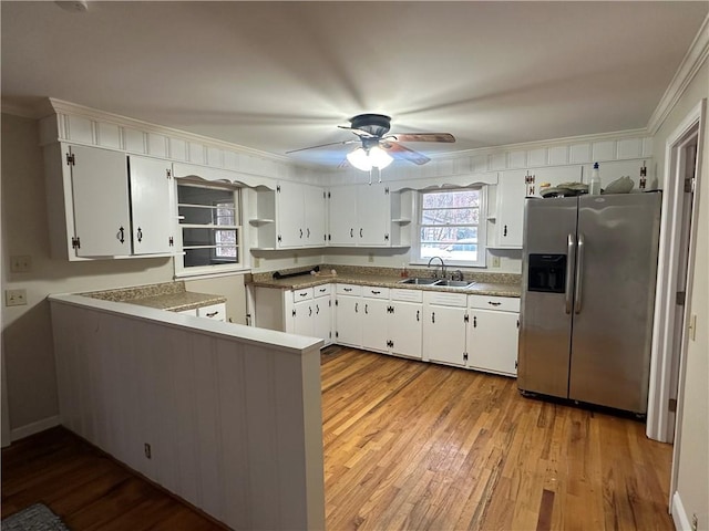 kitchen featuring white cabinets, crown molding, sink, stainless steel fridge, and kitchen peninsula