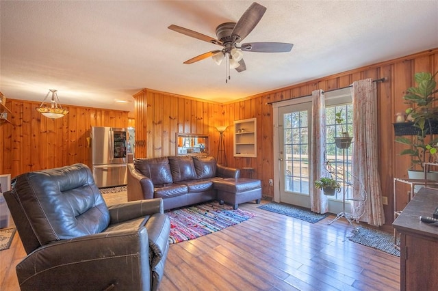 living room with hardwood / wood-style flooring, ceiling fan, and wooden walls