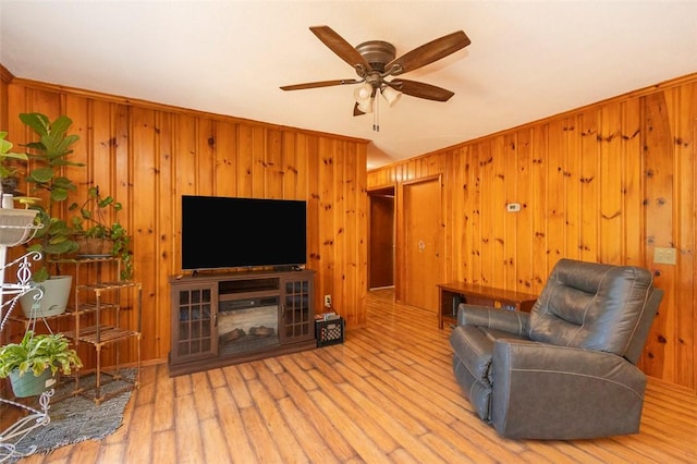 living room featuring light hardwood / wood-style floors, ceiling fan, and wooden walls