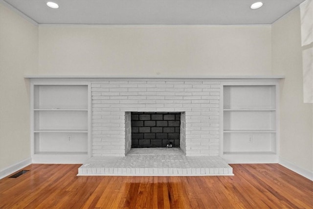 room details with hardwood / wood-style floors, built in shelves, and a brick fireplace