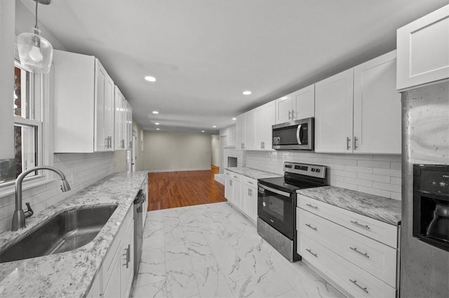 kitchen featuring white cabinetry, sink, stainless steel appliances, light stone counters, and decorative light fixtures