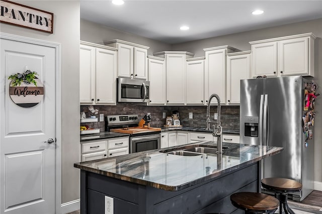 kitchen featuring sink, backsplash, an island with sink, a kitchen bar, and appliances with stainless steel finishes