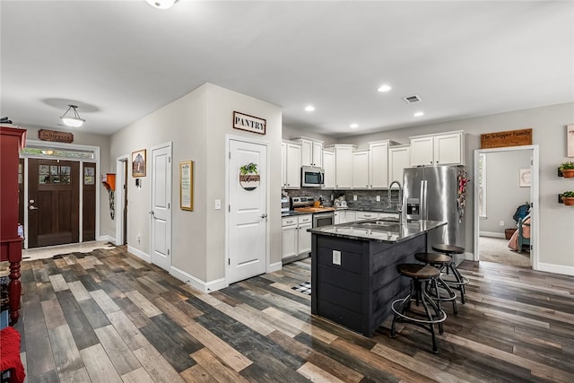 kitchen featuring a kitchen island with sink, white cabinets, a kitchen breakfast bar, dark hardwood / wood-style floors, and stainless steel appliances