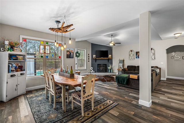 dining space featuring ceiling fan, a large fireplace, dark hardwood / wood-style floors, and vaulted ceiling