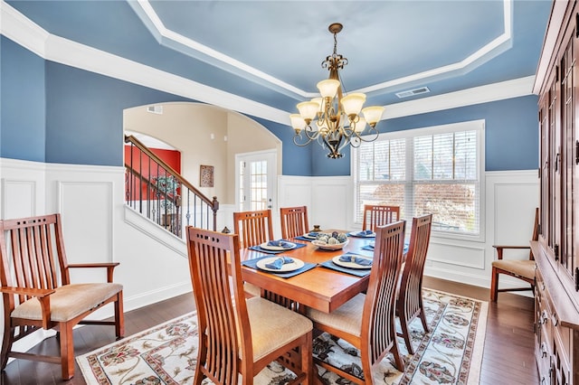 dining area featuring dark wood-type flooring, a raised ceiling, a notable chandelier, and crown molding