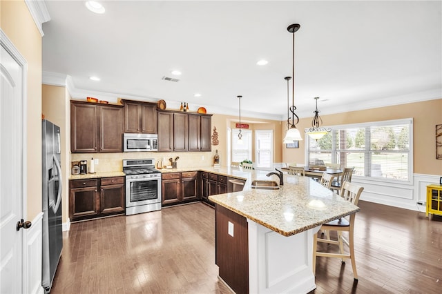 kitchen featuring appliances with stainless steel finishes, light stone counters, crown molding, decorative light fixtures, and a breakfast bar area