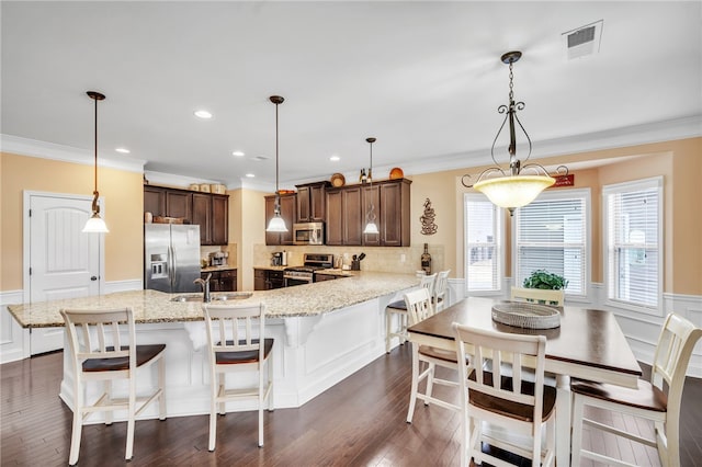 kitchen featuring sink, stainless steel appliances, crown molding, pendant lighting, and a kitchen bar