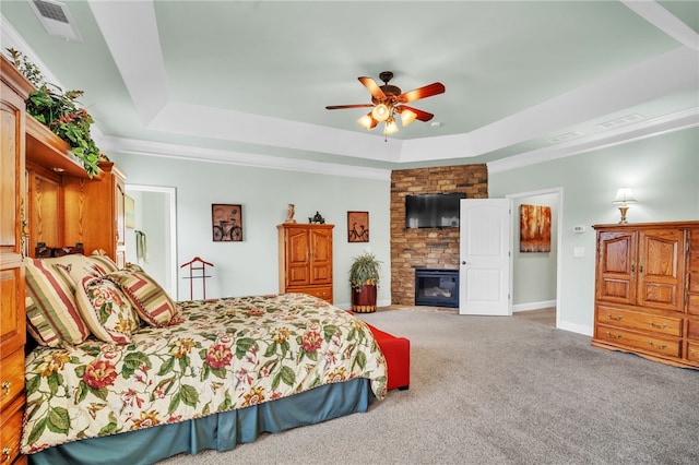 carpeted bedroom with ceiling fan, a raised ceiling, a fireplace, and crown molding