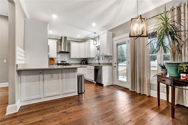 kitchen with light stone countertops, stainless steel appliances, wall chimney range hood, white cabinets, and hanging light fixtures