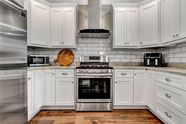 kitchen with decorative backsplash, stainless steel appliances, white cabinetry, and wall chimney range hood