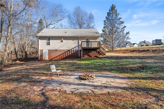 rear view of property featuring a lawn, a wooden deck, and a fire pit