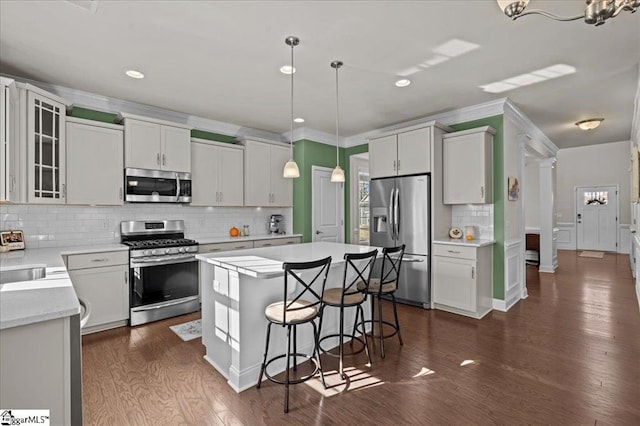 kitchen with appliances with stainless steel finishes, dark hardwood / wood-style flooring, white cabinets, a kitchen island, and hanging light fixtures