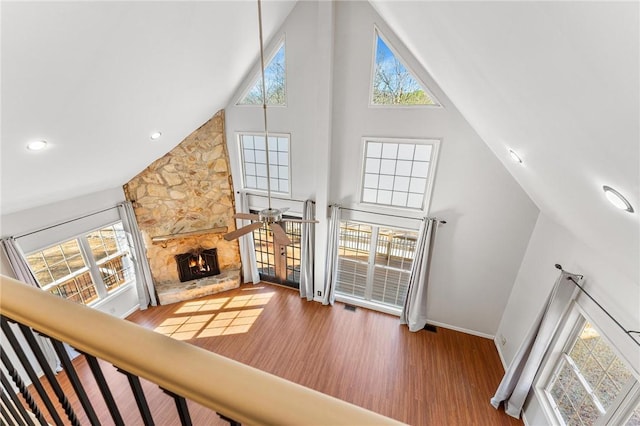 living room with a healthy amount of sunlight, high vaulted ceiling, a stone fireplace, and hardwood / wood-style floors