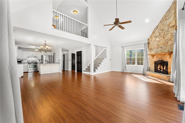 unfurnished living room with hardwood / wood-style flooring, a stone fireplace, high vaulted ceiling, and ceiling fan