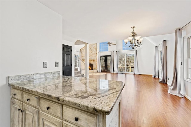 kitchen with an inviting chandelier, light hardwood / wood-style flooring, pendant lighting, light stone countertops, and cream cabinets