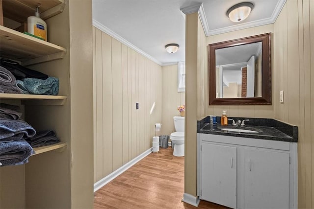 bathroom featuring toilet, vanity, wooden walls, crown molding, and hardwood / wood-style flooring