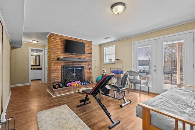 workout area with french doors, a brick fireplace, and wood-type flooring