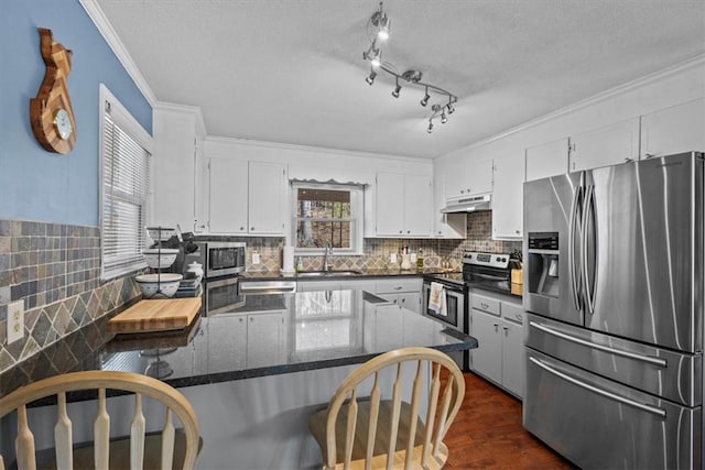 kitchen with appliances with stainless steel finishes, white cabinets, sink, kitchen peninsula, and ornamental molding