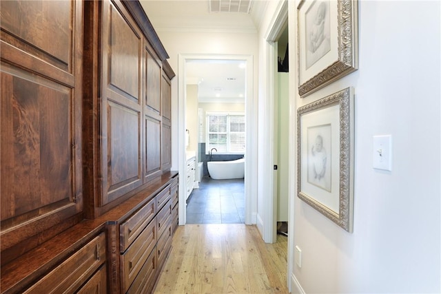 corridor with light wood-type flooring and crown molding