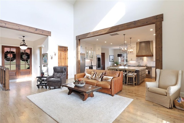 living room with beam ceiling, light hardwood / wood-style flooring, a towering ceiling, and a notable chandelier