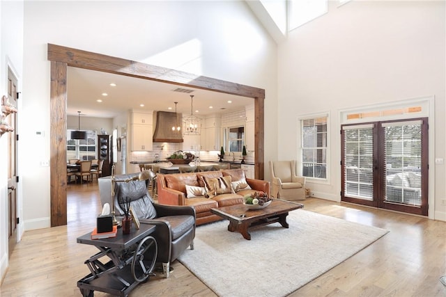 living room featuring french doors, a towering ceiling, light hardwood / wood-style flooring, and a chandelier