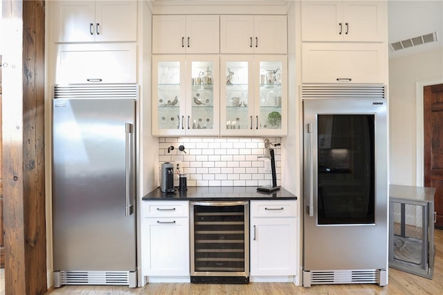 bar featuring high end refrigerator, stainless steel built in fridge, wine cooler, tasteful backsplash, and white cabinetry