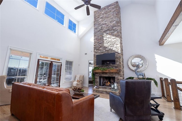 living room featuring ceiling fan, a stone fireplace, beamed ceiling, high vaulted ceiling, and light wood-type flooring