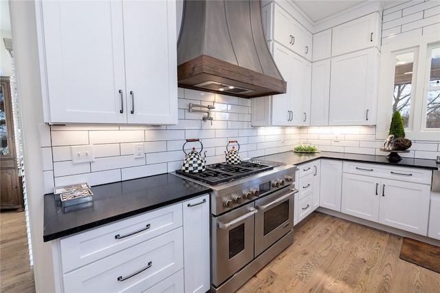 kitchen featuring decorative backsplash, light wood-type flooring, custom range hood, range with two ovens, and white cabinets