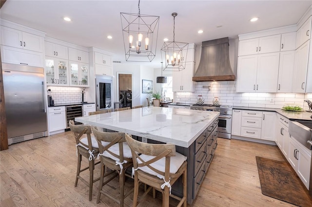 kitchen featuring premium appliances, premium range hood, white cabinetry, and a spacious island