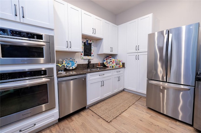 kitchen featuring sink, light hardwood / wood-style flooring, dark stone countertops, white cabinetry, and stainless steel appliances