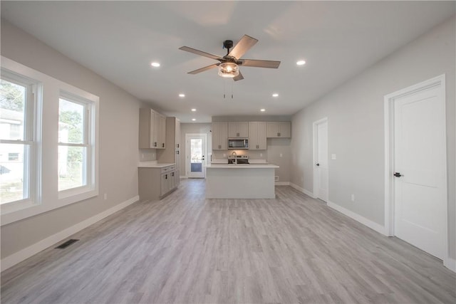 interior space with stainless steel appliances, gray cabinets, a kitchen island with sink, and light hardwood / wood-style flooring