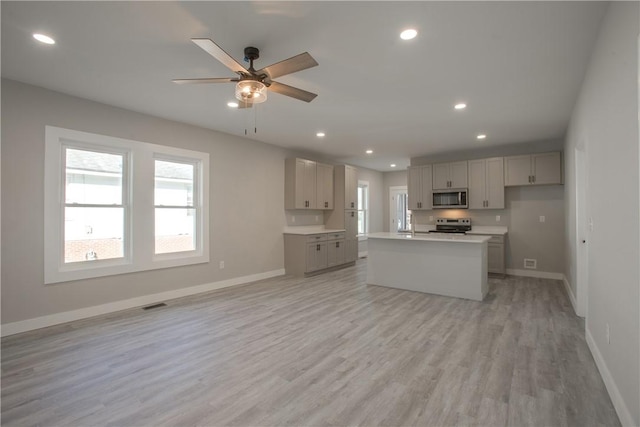 kitchen with a center island with sink, ceiling fan, gray cabinets, light hardwood / wood-style floors, and stainless steel appliances