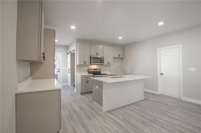 kitchen featuring appliances with stainless steel finishes, gray cabinetry, sink, a center island with sink, and light hardwood / wood-style floors