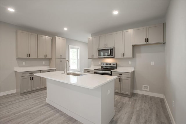 kitchen featuring a kitchen island with sink, sink, gray cabinets, light hardwood / wood-style floors, and stainless steel appliances