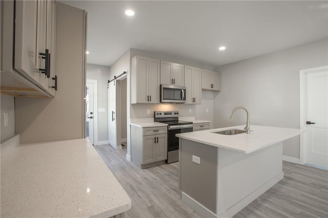 kitchen with sink, stainless steel appliances, a barn door, light hardwood / wood-style floors, and a kitchen island with sink