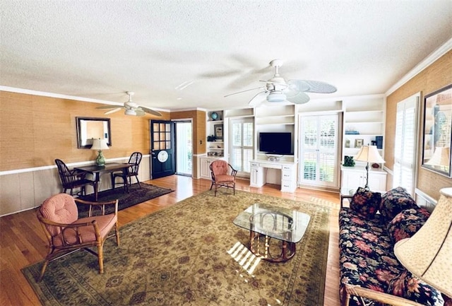 living room featuring built in features, wood-type flooring, a textured ceiling, and ornamental molding