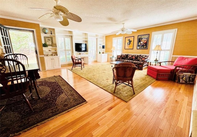 living room with built in shelves, light hardwood / wood-style floors, a textured ceiling, and ceiling fan