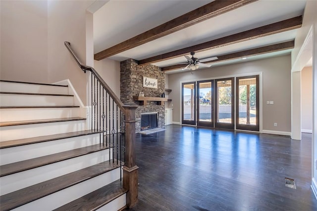 unfurnished living room featuring baseboards, stairs, a stone fireplace, wood finished floors, and a ceiling fan