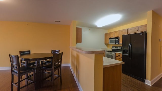 kitchen featuring a kitchen breakfast bar, kitchen peninsula, dark wood-type flooring, and stainless steel appliances