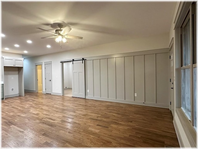 spare room featuring ceiling fan, a barn door, and wood-type flooring