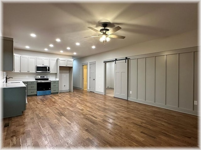 kitchen featuring ceiling fan, sink, stainless steel appliances, a barn door, and white cabinets