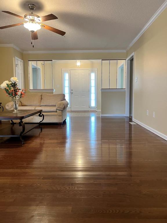 unfurnished living room with crown molding, ceiling fan, dark hardwood / wood-style flooring, and a textured ceiling