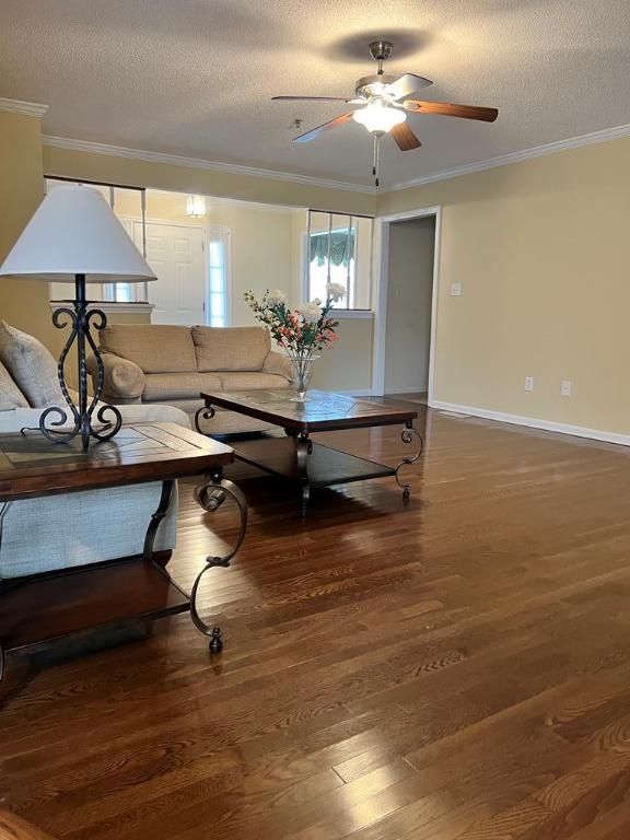 living room featuring dark hardwood / wood-style floors, ceiling fan, ornamental molding, and a textured ceiling