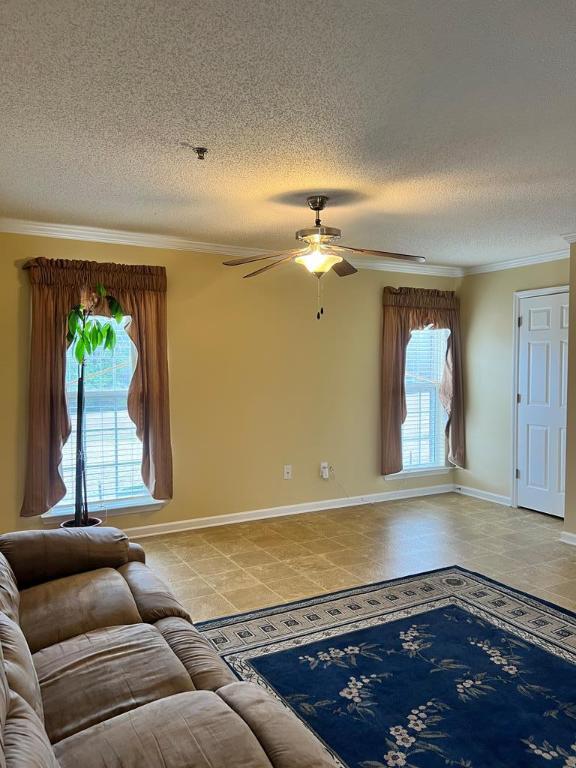 unfurnished living room featuring ceiling fan, a textured ceiling, and ornamental molding