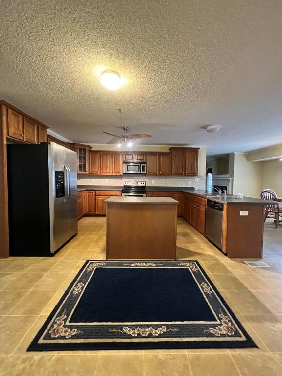 kitchen with a center island, ceiling fan, a textured ceiling, appliances with stainless steel finishes, and kitchen peninsula