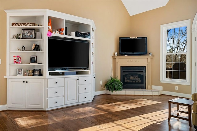 living room featuring vaulted ceiling, dark wood-type flooring, and a tiled fireplace